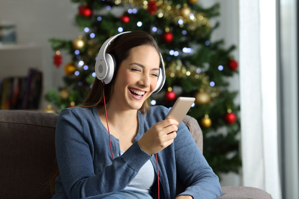 Woman listening to music with headphones on in front of Christmas tree